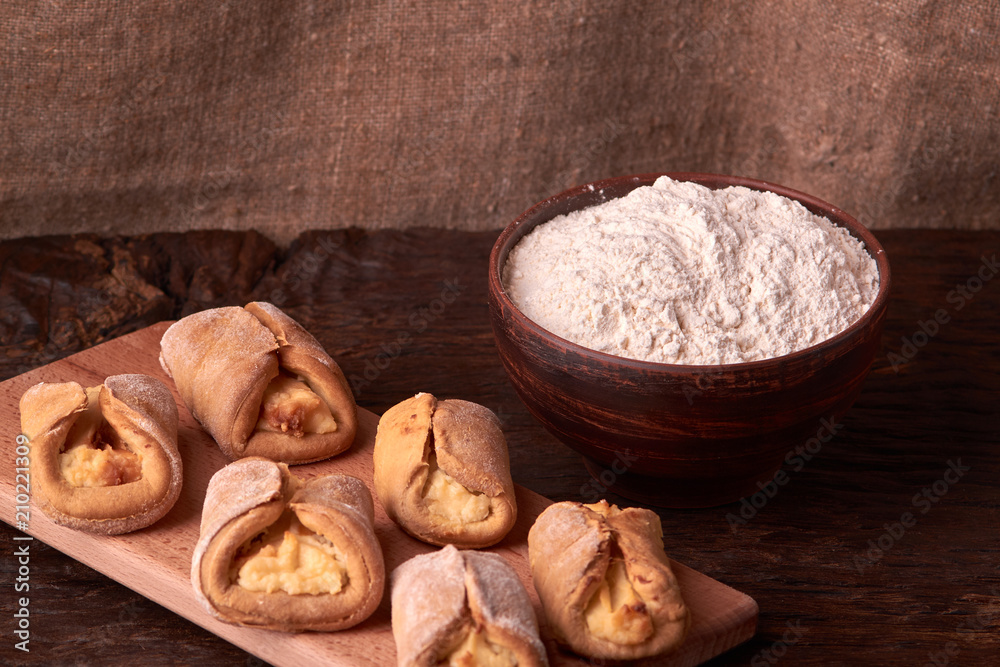Fototapeta premium flour in clay bowl products for making cheesecakes on a wooden chopping board. Homemade Cottage cheese cookies on black background. still life composition