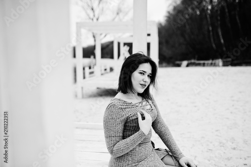 Portrait of brunette girl in gray dress sitting at white wooden construction.