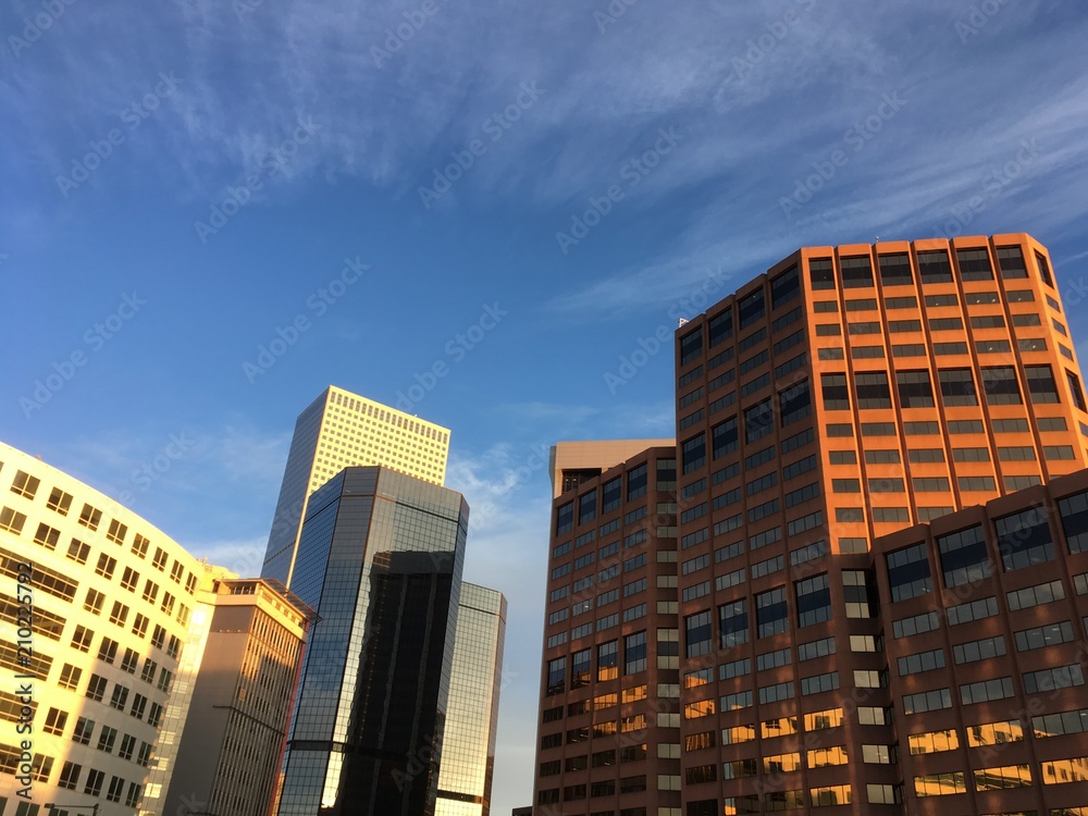 Group of office buildings in the business district of Denver at sunrise. Warm light shining on skyscrapers in downtown Denver Colorado USA. Blue sky with wispy clouds.