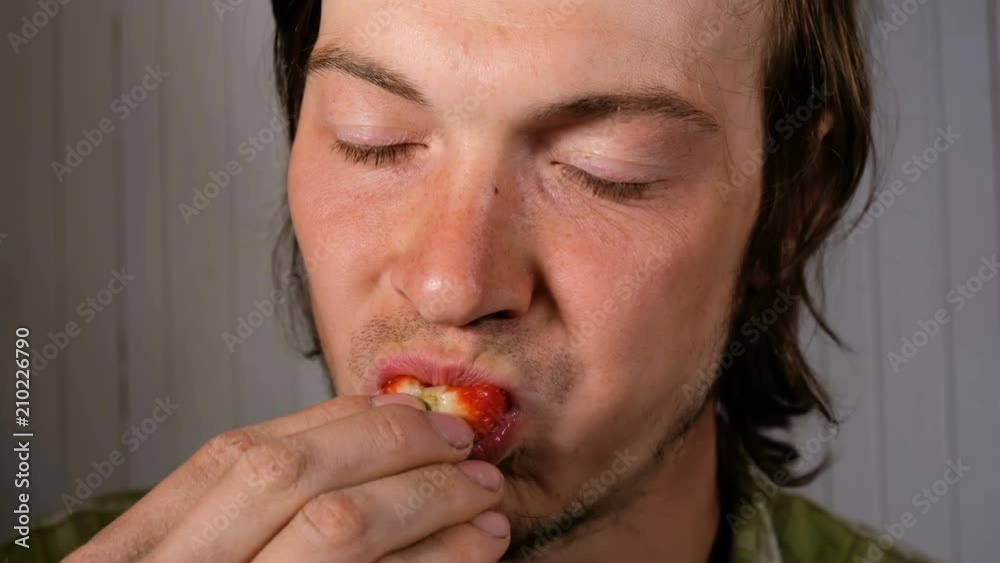 Young european man is appetizing eats a strawberry close-up Young european man is appetizing eats a strawberry close-up
