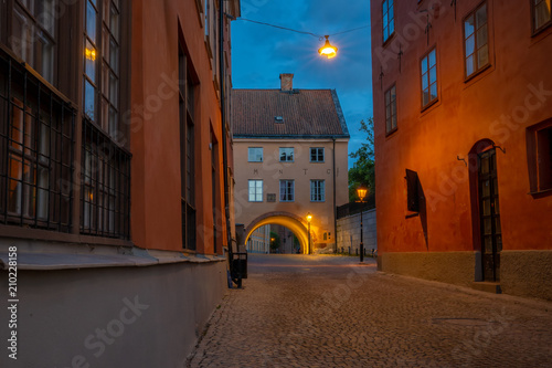 Fototapeta Naklejka Na Ścianę i Meble -  View of a small street or alley in the old town of the university city Uppsala, Sweden. It is almost midnight but the summer sky, a deep blue nuance, is still bright. Street lamps add deep amber light