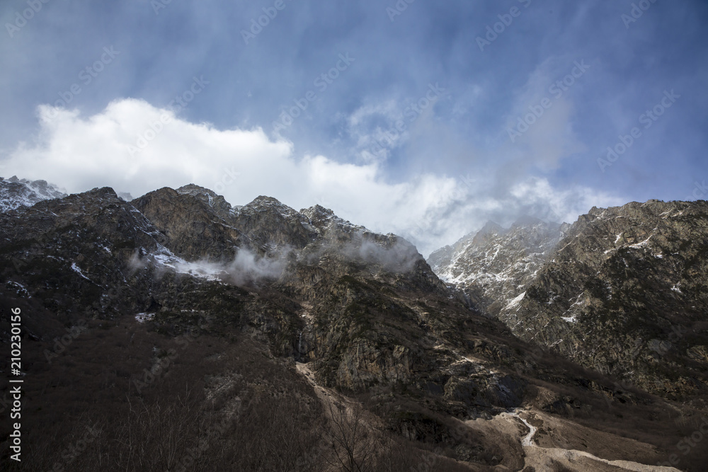 Горный пейзаж. Вершины в белых облаках, Красивый вид на живописное ущелье, панорама с высокими горами. Природа Северного Кавказа, отдых в горах