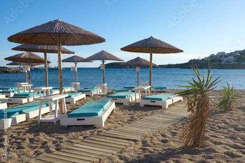 Umbrellas with sunbeds on beautiful sandy beach with turquoise sea water in picturesque village of Batsi, Andros island, Cyclades, Greece