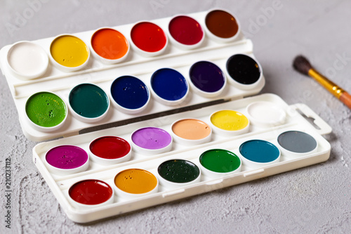 Set of watercolor paints, brushes for painting and blank white paper sheet of sketchbook on Concrete surface texture background.