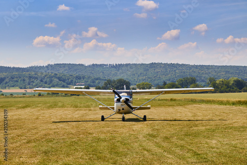 Front view of Cessna 172 airplane standing on grass field with blue cloudy sky on the background. photo