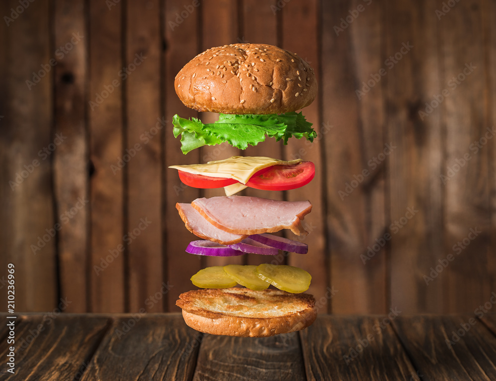 Fresh sandwich with flying ingredients isolated on wooden background