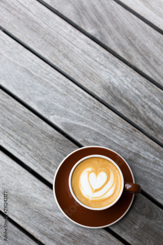 Dark red cup of cappuccino with the heart shape latte-art on wood background