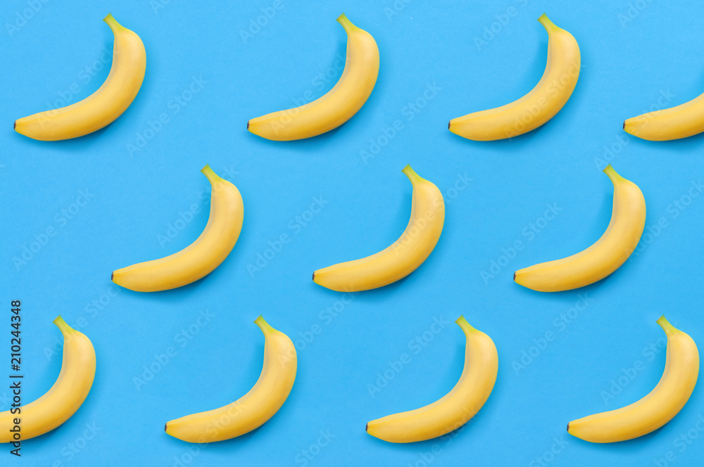 Minimalist pattern, fresh fruit and colorful art concept with flat lay top view of multiple yellow bananas isolated on bright blue background