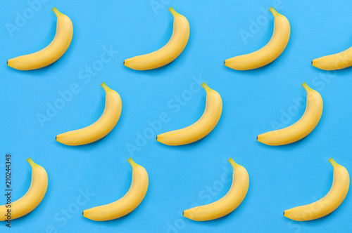 Minimalist pattern, fresh fruit and colorful art concept with flat lay top view of multiple yellow bananas isolated on bright blue background