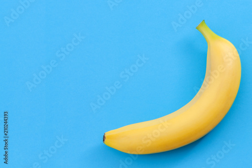 Minimalist pattern, fresh fruit and colorful art concept with flat lay top view of single yellow banana isolated on bright blue background with copy space