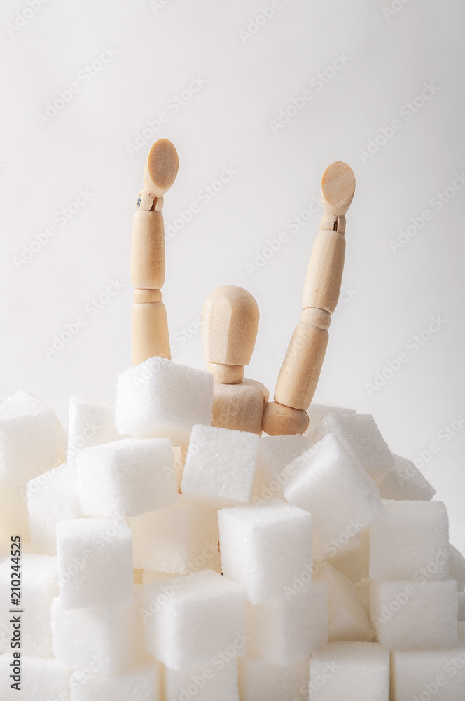 Sugar addiction, insulin resistance, unhealthy diet and November 14 is diabetes awareness day concept with a puppet drowning in sugar cubes isolated on white background and copy space for text