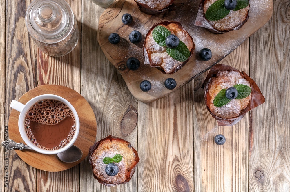 Muffins with blueberries and a cup of hot chocolate on a wooden background. homemade baking. Top view Muffins with blueberries and a cup of hot chocolate on a wooden background. homemade baking. Top view