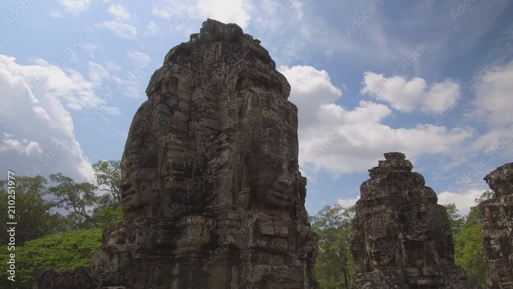 Spectacular ancient monuments with faces on each side fade in the sunny tropical nature. Beautiful religious monuments slowly decaying in world famous Angkor Wat temple complex. Stunning architecture. Spectacular ancient monuments with faces on each side fade in the sunny tropical nature. Beautiful religious monuments slowly decaying in world famous Angkor Wat temple complex. Stunning architecture.