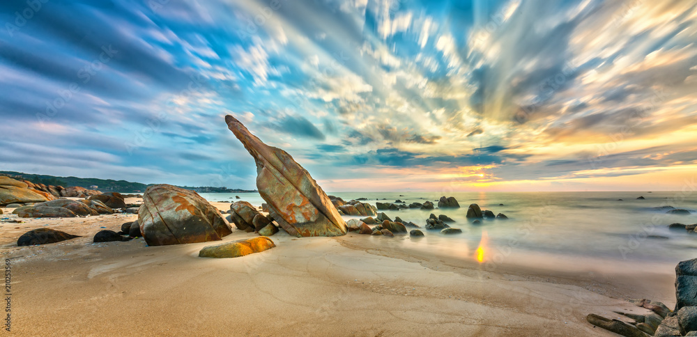 Fototapeta premium Volcanic rocks beach in sunrise with dramatic sky, below reefs are interspersed waves undulating smooth real welcome new day beautiful