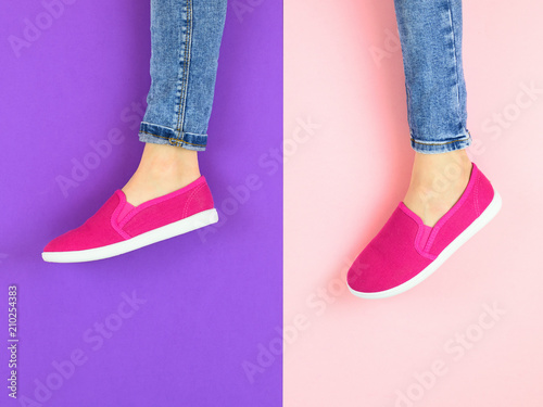 Legs of the girl in red sneakers and jeans on the purple and pink floor. The view from the top.