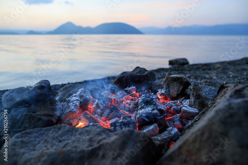 Glowing ashes smoldering in a stone fire ring on the shore of Lake Koya in Hokkaido, Japan