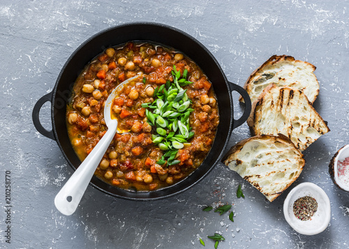 Vegetarian mushrooms chickpea stew in a iron pan and rustic grilled bread on a gray background, top view. Healthy vegetarian food concept. Vegetarian chili photo