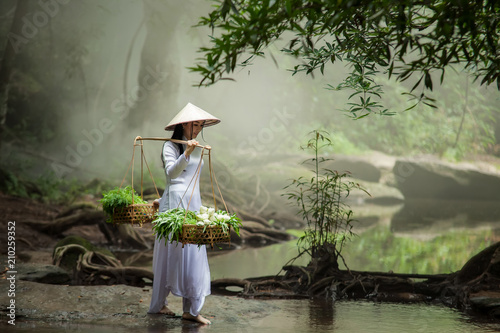 Beautiful woman wearing a hat Dress Ao Dai traditional Vietnamese dress standing in the forest. photo