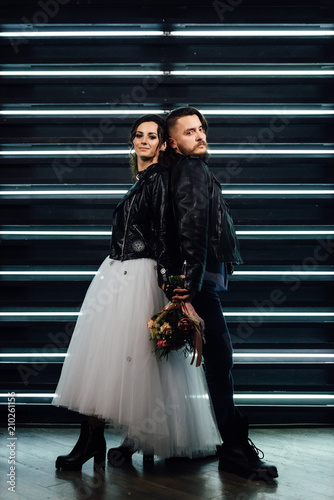 Wedding in the style of rock. Rocker or Biker wedding. Guys with stylish leather jackets. It's a rock'n'roll baby Sweet couple in a photo studio. Steep shooting with mirrors and lamps.