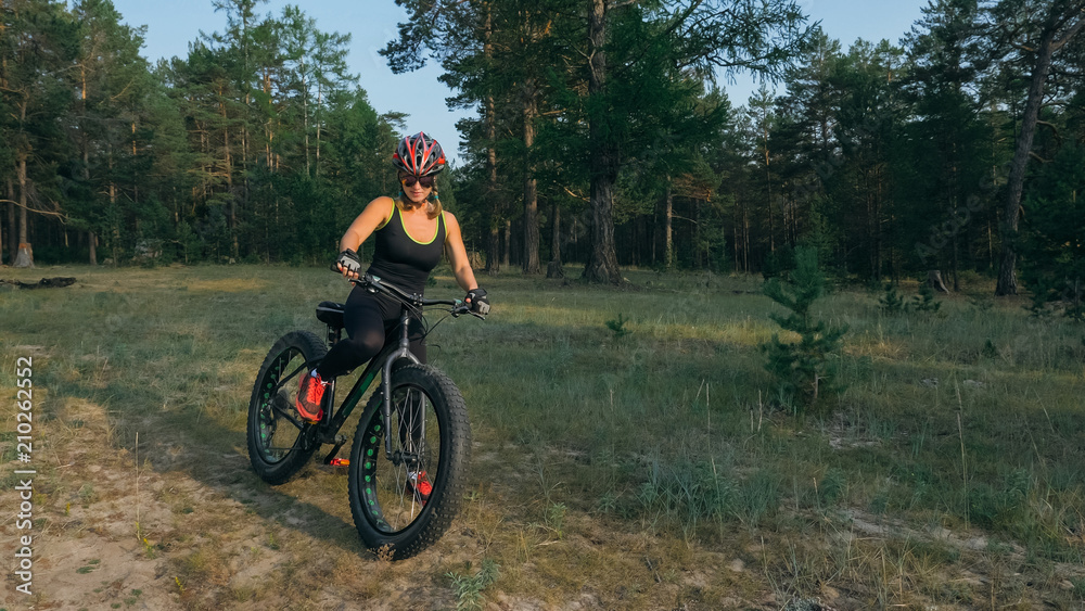 Fototapeta premium Fat bike also called fatbike or fat-tire bike in summer riding in the forest. Beautiful girl and her bicycle in the forest. She rolls her bike and poses to the operator.