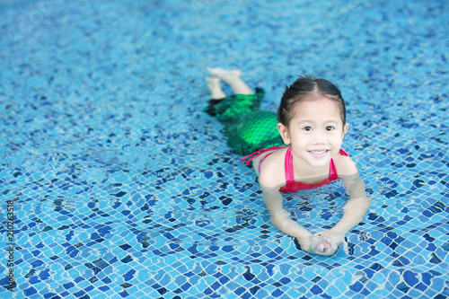 Fotografie Portrait of cute little Asian child girl wear mermaid swimming suit has fun at the pool