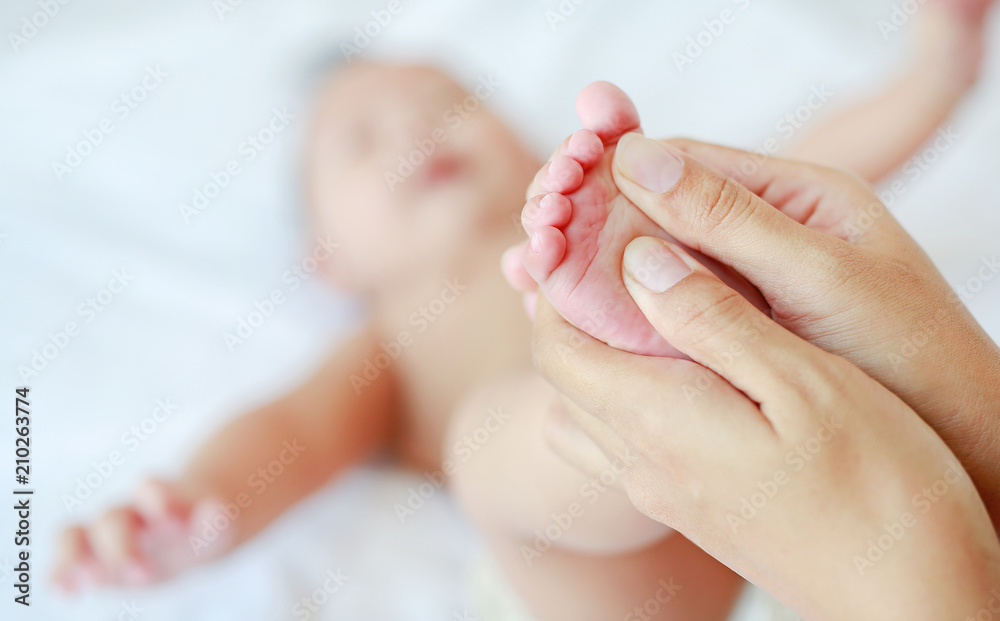 Mother hand massaging feet of infant baby on the bed at home. Mother hand massaging feet of infant baby on the bed at home.
