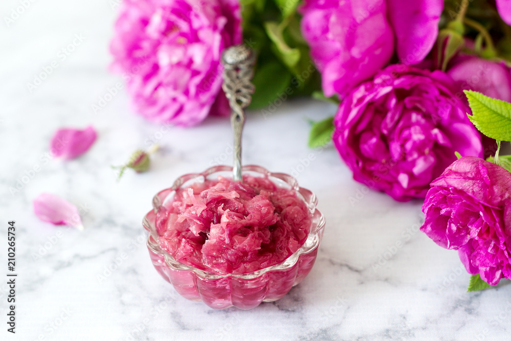 Jam with rose petals in a glass bowl and bright roses on a light background. Jam with rose petals in a glass bowl and bright roses on a light background.