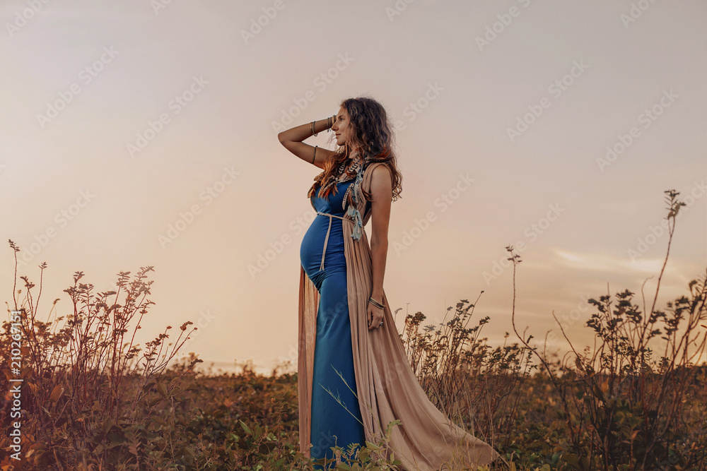 happy pregnant woman walking on a field at sunset - obrazy, fototapety, plakaty 