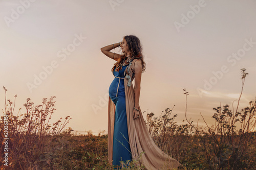 happy pregnant woman walking on a field at sunset