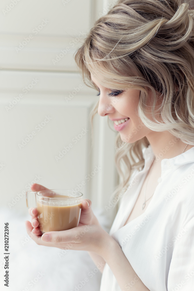 beautiful cute girl near the window in the morning in a white shirt with a cup of coffee beautiful cute girl near the window in the morning in a white shirt with a cup of coffee