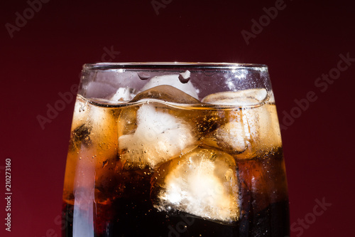 A glass of cola beverage with a salt. On a red background.