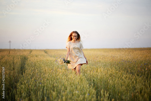 girl with flowers walking on a grain field. © makam1969