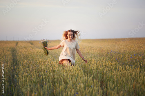 girl with flowers walking on a grain field.