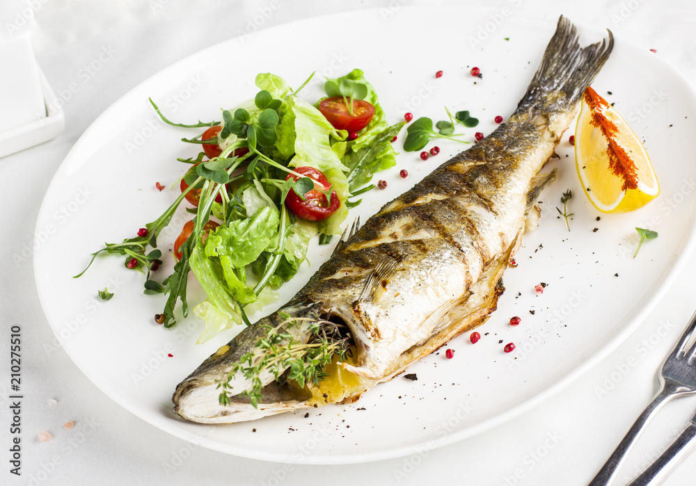 Baked fish with lemon and fresh vegetables on a white plate in the restaurant Baked fish with lemon and fresh vegetables on a white plate in the restaurant