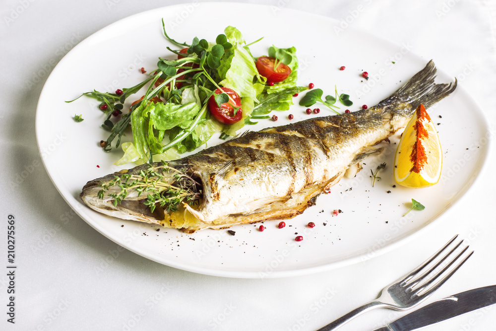 Baked fish with lemon and fresh vegetables on white plate Baked fish with lemon and fresh vegetables on white plate