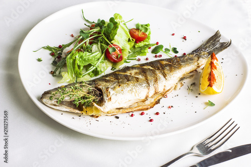 Baked fish with lemon and fresh vegetables on white plate