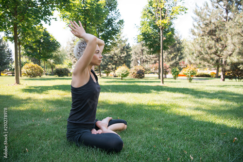 side view of woman practicing yoga in lotus pose with raised hands making namaste gesture on grass in park © LIGHTFIELD STUDIOS