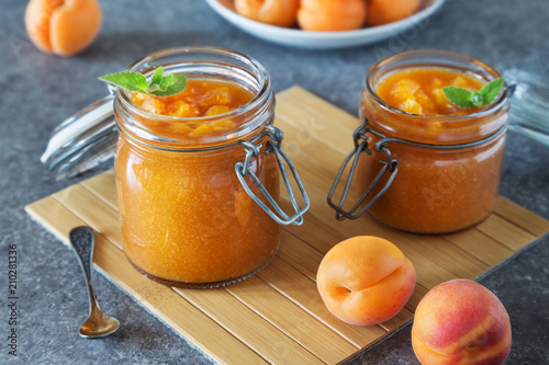 Jar of apricot jam with spoon and fruit on grey table