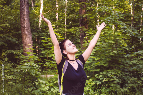 a beautiful girl stands in the forest and rejoices, holding her hands up