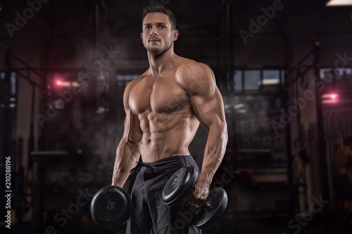 Murais de parede Young handsome sportsman bodybuilder weightlifter with an ideal body, after coaching poses in front of the camera, abdominal muscles, biceps triceps