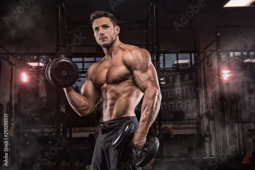 Obraz Młody przystojny sportowiec kulturysta w podnoszeniu ciężarów z idealnym ciałem, po treningu stawia przed kamerą, mięśnie brzucha, biceps triceps. W odzieży sportowej.