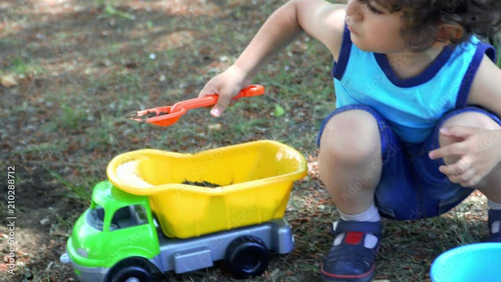 Cute little boy playing with big toy truck in the park. 4K Cute little boy playing with big toy truck in the park. 4K