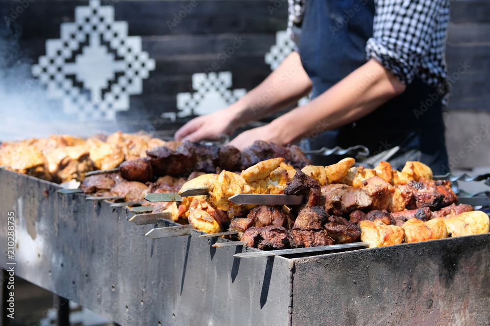 Tasty fried pieces of meat on skewers are roasted on grill at festival outdoor. Chef in black apron prepares barbecue. Shish kebab national cuisine of Central Asia.