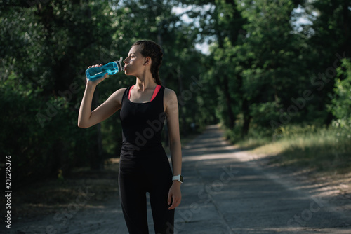 attractive sportswoman drinking water in park