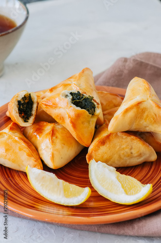 Arabic and middle eastern food concept. Fatayer sabanekh - traditional arabic spinach triangle hand pies  on a white stone background. photo