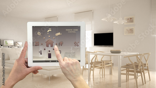 Smart remote home control system on a digital tablet. Device with app icons. Minimalist modern bright living room in the background, architecture interior design