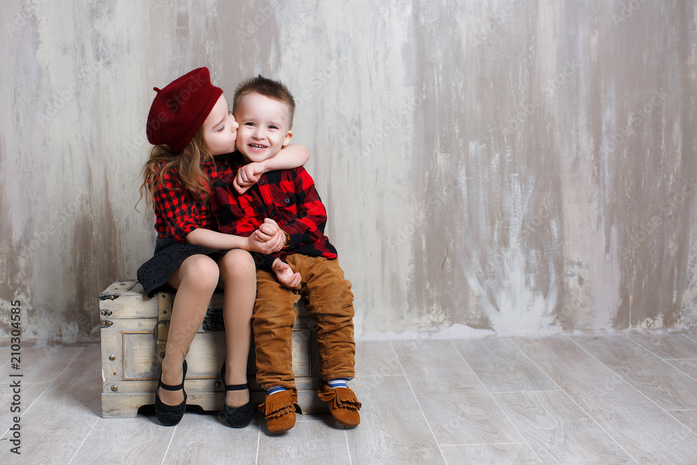 Cute stylish kids on grey Studio background. Little girl and boy sitting  together on an old