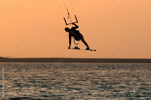 Kite surfing girl in sexy swimsuit with kite in sky on board in blue sea riding waves with water splash. Recreational activity, water sports, action, hobby and fun in summer time. Kiteboarding sport