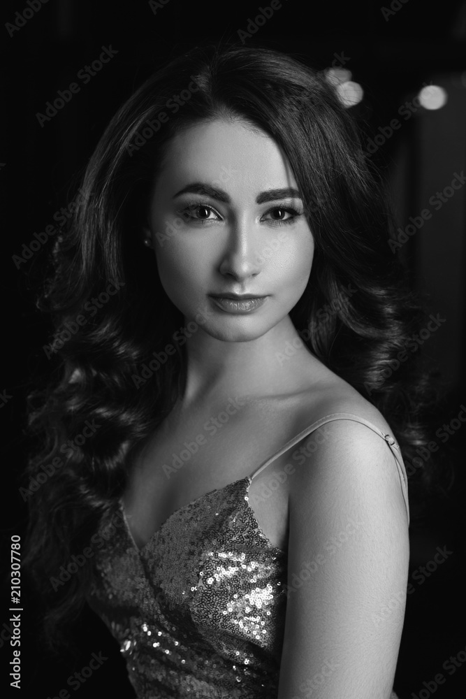 Breast portrait of young beautiful caucasian woman in evening shining dreess with perfect makeup and long wavy brunette hair looking at you.