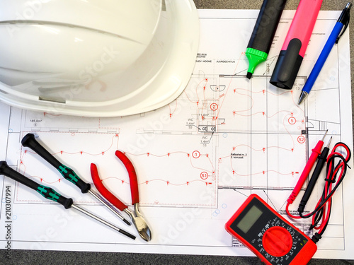 Office table or desk with the project drawings of the security or fire alarm system, a protective helmet, tools, a multimeter and markers.